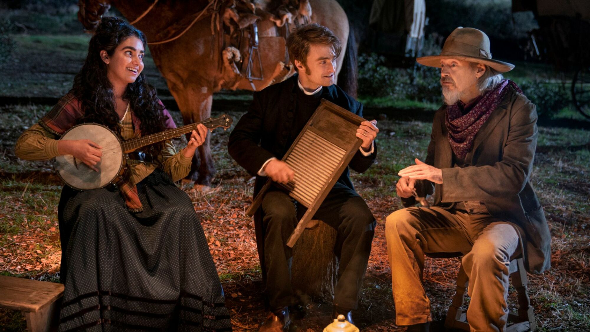 Three people play music around a campfire in the Western.